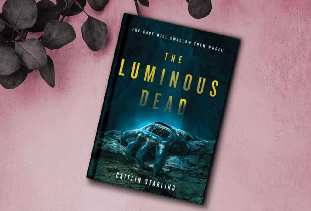 The cover for The Luminous Dead by Caitlin Starling. The cover features a hand wearing a sci-fi glove reaching over the edge of a cliff.