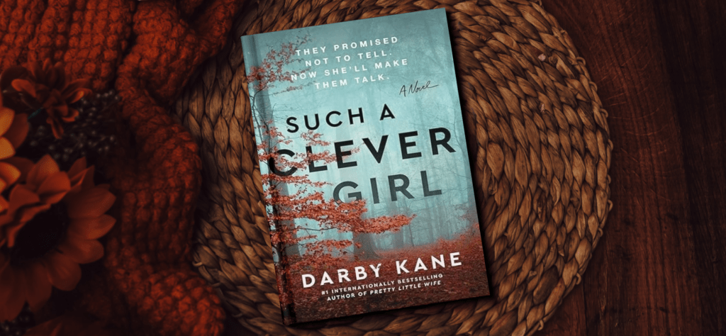 The book cover for Such a Clever Girl by Darby Kane. The cover features a misty forest and a forest floor blanketed with autumn leaves. The background features a warm orange blanket.
